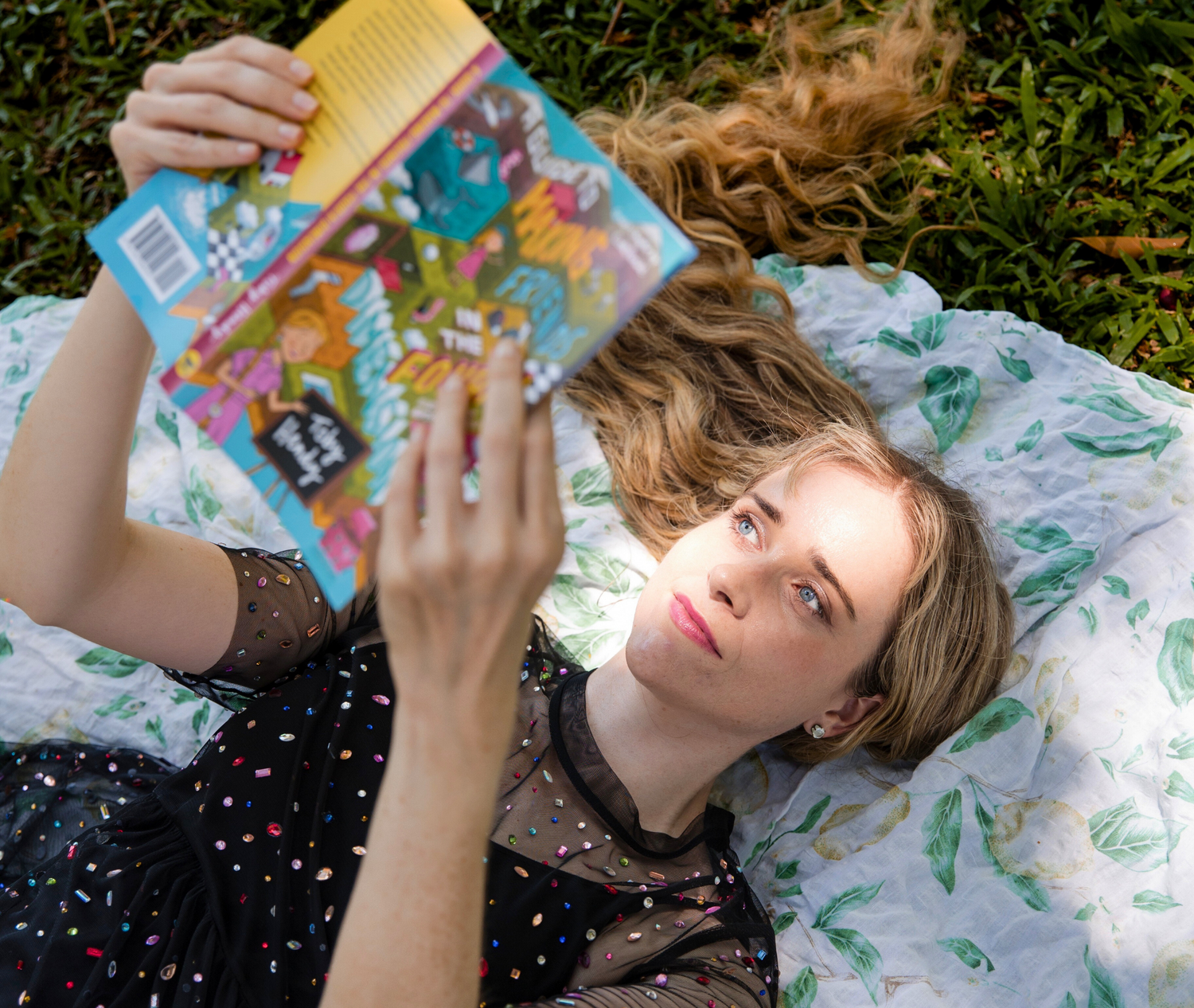 Woman lying on a blanket outdoors, holding a colorful book