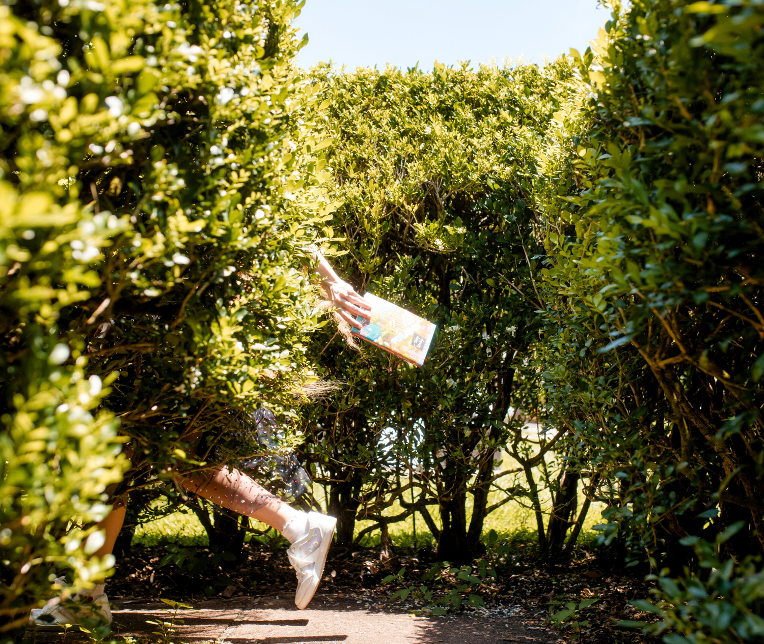 Person holding a book in a garden with greenery